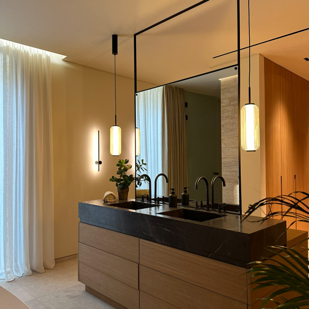 Bespoke vanity unit in iroko wood with natural stone washbasins, bespoke metal framed, double sided mirror and Aromas del Campo Elma pendant lights.