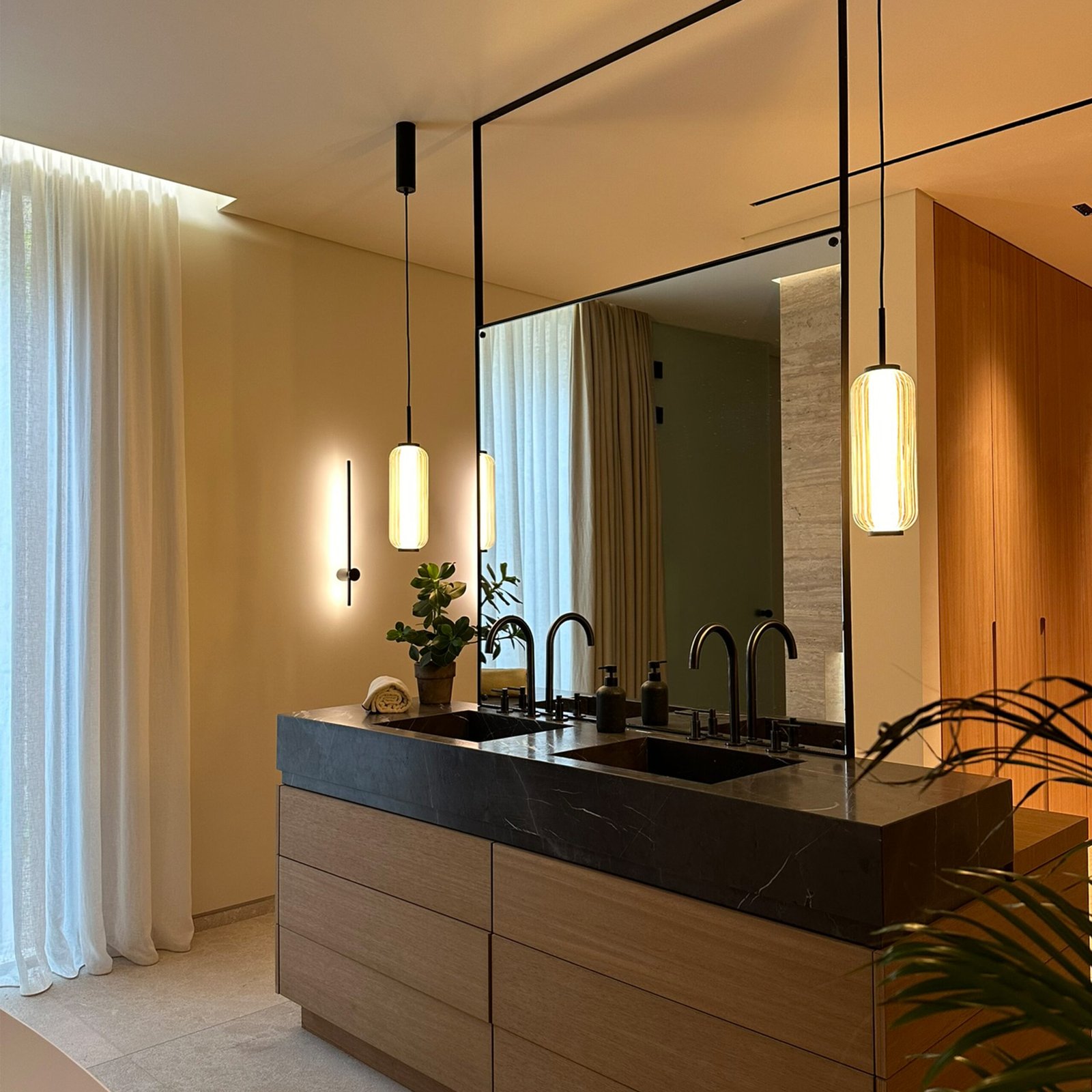 Bespoke vanity unit in iroko wood with natural stone washbasins, bespoke metal framed, double sided mirror and Aromas del Campo Elma pendant lights.
