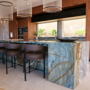Bespoke kitchen island clad in blue quartzite stone with gold veining. Praddy Bamboo bar stools in tobacco brown leather. Vibia Array pendant lights.