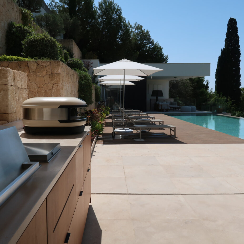 View of outdoor area with Gozney Pizza Oven, Beefeater Barbecue, sunbeds, umbrellas and pool in the distance.