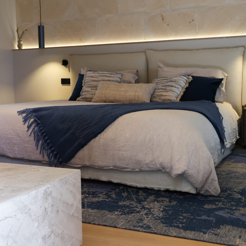 Main bedroom with upholstered bed base and headboard from Acanapiel. Lights by Onok and Aromas del Campo. The rug echoes the colours of the Santa Maria del Cami Church Tower.